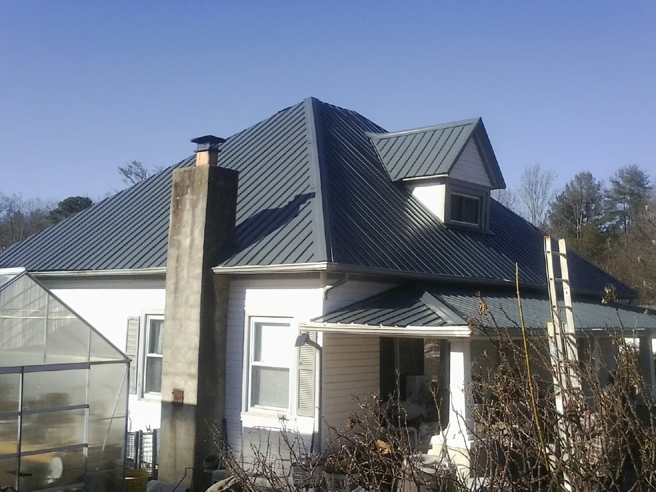 Dark blue standing seam metal roof on a white farmhouse with dormer — Slate & Tile Roof Repair by Roofing Brothers in Albertville