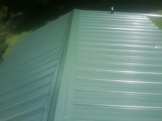 New green metal panels meeting at the ridge of a roof — Flat Roof Repair work by our crew in Albertville