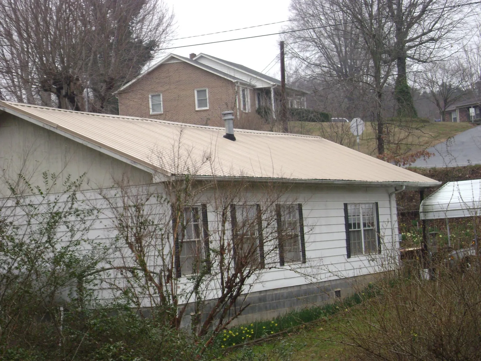 Tan metal roof on a white sided house set into a hillside — Commercial Roofing by Roofing Brothers in Albertville