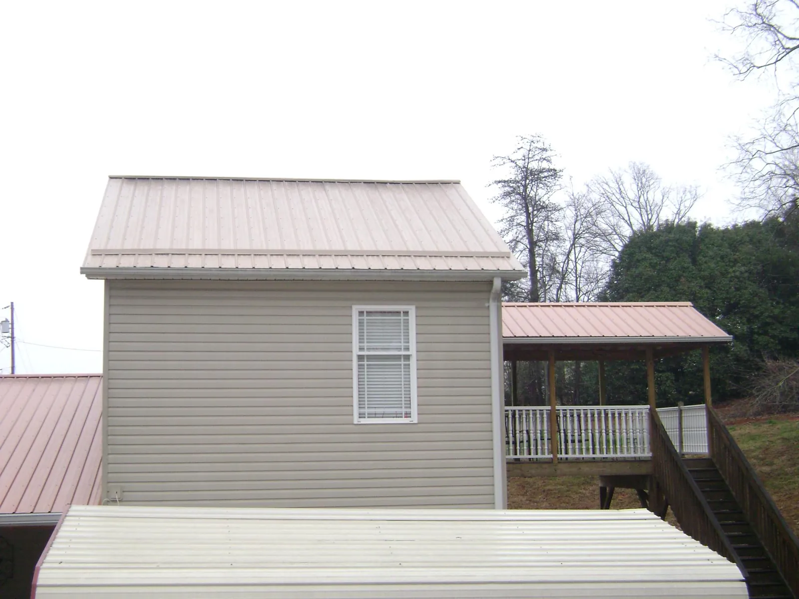 Tan metal roofs on a two story addition and attached porch, from a Roof Replacement job in Albertville